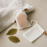 Two white exfoliating soap bags with a persimmon soap bar inside one of them
